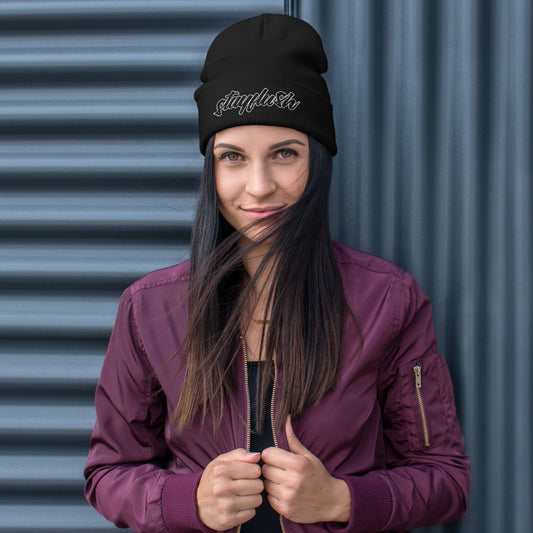 Smiling as their hair blows in the wind, a person wears a black, form-fitting StayFlush Beanie with “Stylish” embroidered on it and a maroon jacket—a perfect breathable cotton blend accessory for any look.