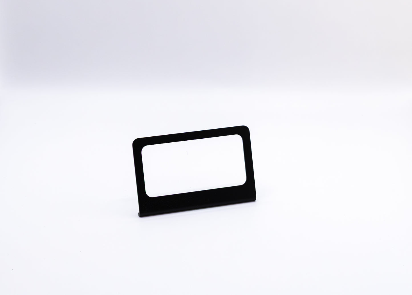 The Switch-Pros 9100 Sidekick Accessory Mount from StayFlush Motorsports, featuring a sleek black rectangular design with a blank white insert, stands centered on a plain white surface against a white background.