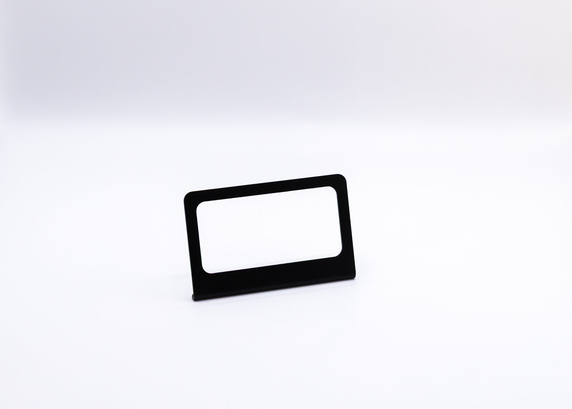 The Switch-Pros 9100 Sidekick Accessory Mount from StayFlush Motorsports, featuring a sleek black rectangular design with a blank white insert, stands centered on a plain white surface against a white background.
