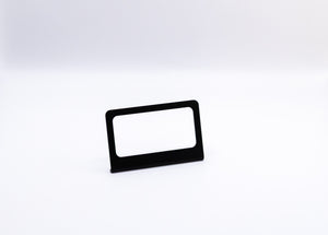 The Switch-Pros 9100 Sidekick Accessory Mount from StayFlush Motorsports, featuring a sleek black rectangular design with a blank white insert, stands centered on a plain white surface against a white background.