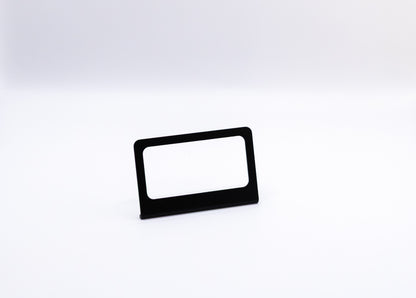 The Switch-Pros 9100 Sidekick Accessory Mount from StayFlush Motorsports, featuring a sleek black rectangular design with a blank white insert, stands centered on a plain white surface against a white background.