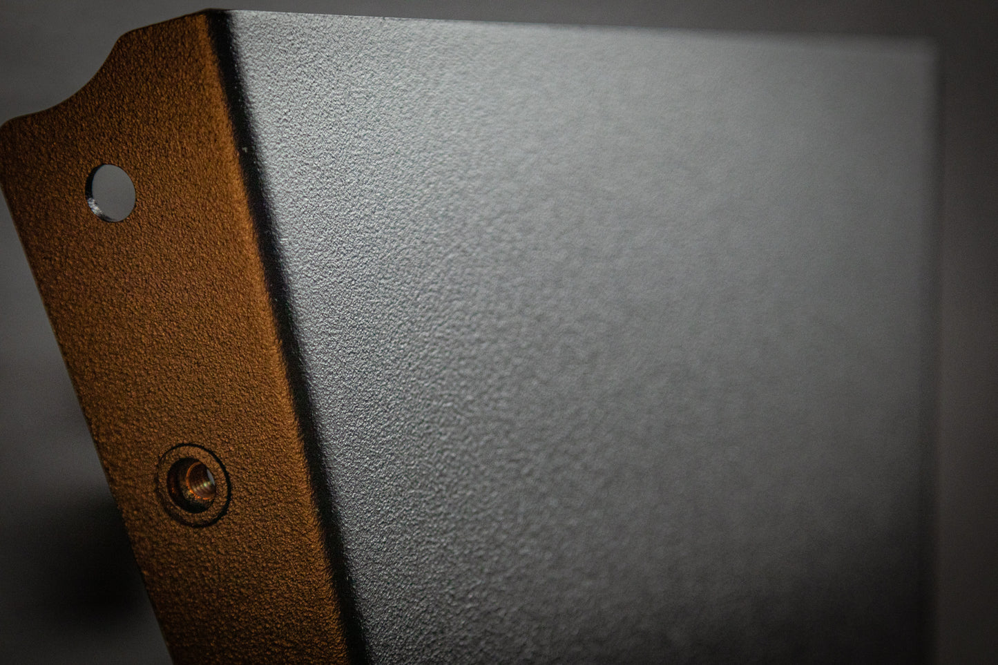 Close-up of the StayFlush Clean Slate Console – Universal Blank Build Platform by StayFlush Motorsports shows its textured dark gray metal, beveled edge, circular hole, and a small screw on one side. Blurred neutral background.
