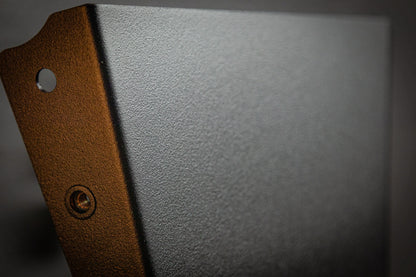 Close-up of the StayFlush Clean Slate Console – Universal Blank Build Platform by StayFlush Motorsports shows its textured dark gray metal, beveled edge, circular hole, and a small screw on one side. Blurred neutral background.